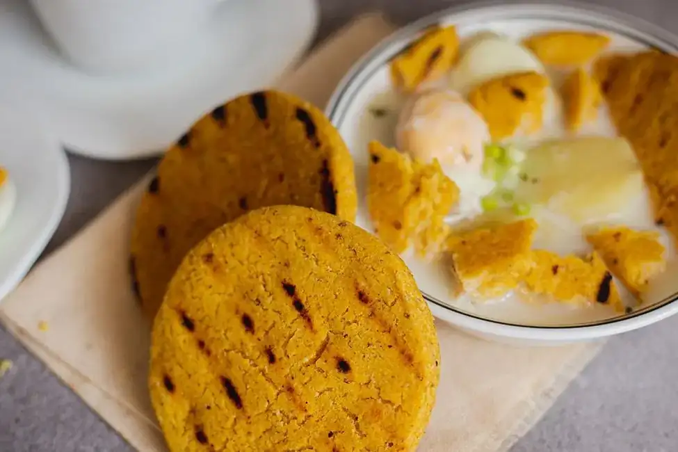 Arepas de maíz amarillo asadas junto a un plato con frutas, en un taller de Barichara