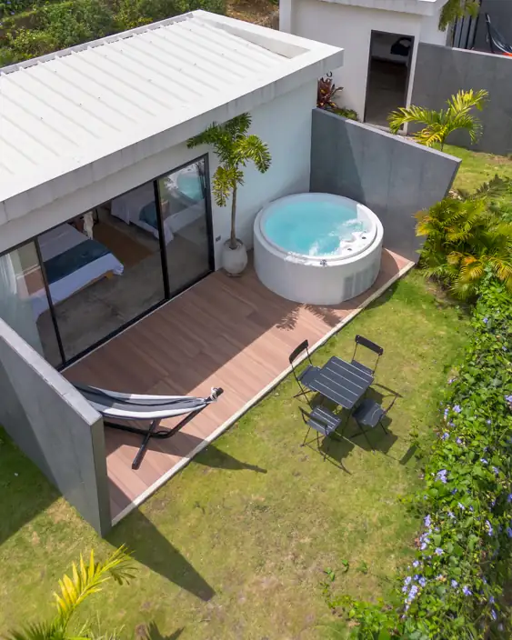 Techo blanco, jacuzzi de agua azul, hamaca y mesa plegable sobre el pasto, tomados desde el dron