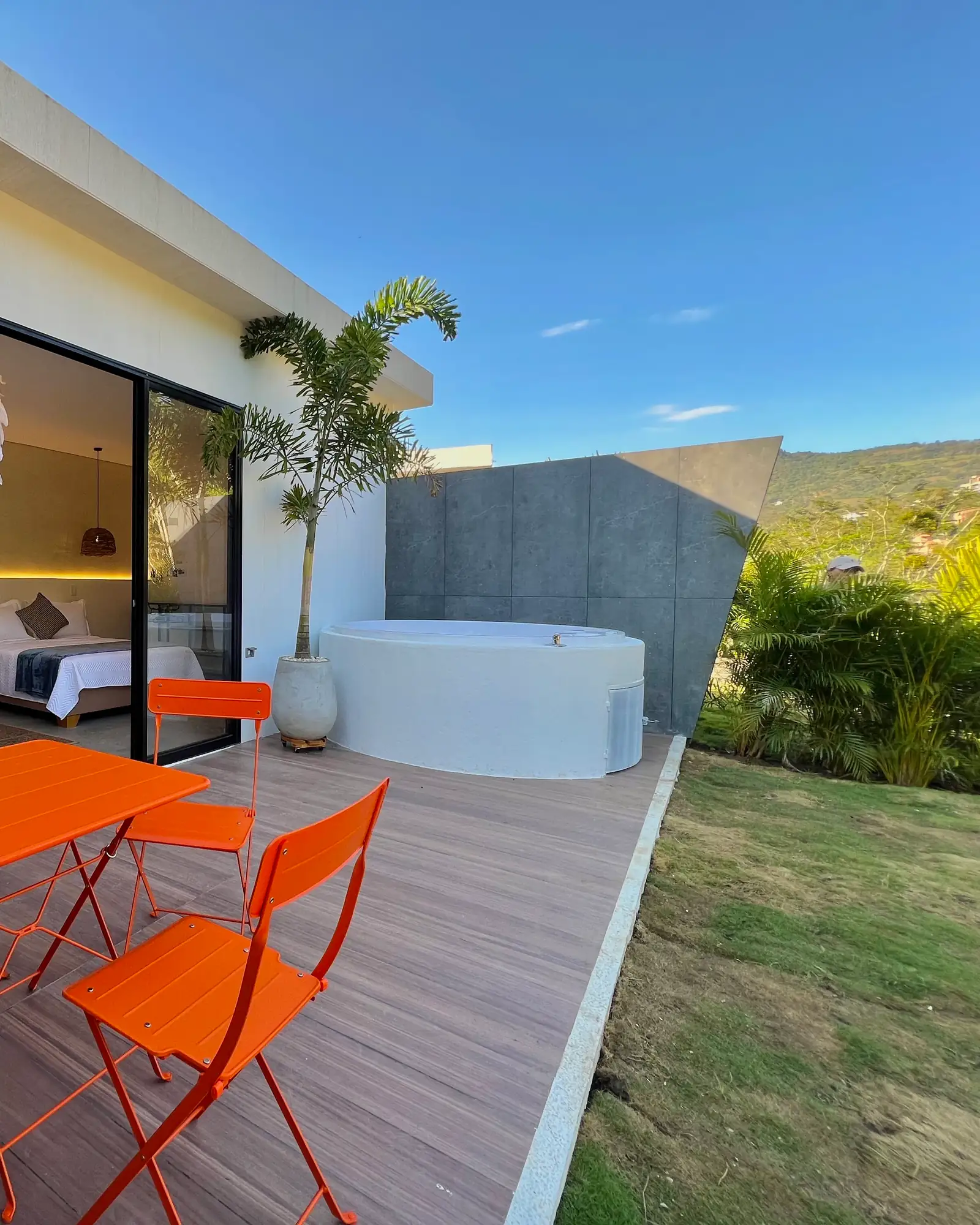 Sillas naranjas y jacuzzi en la terraza de madera del Glamping Familiar, junto al pasto y una palma