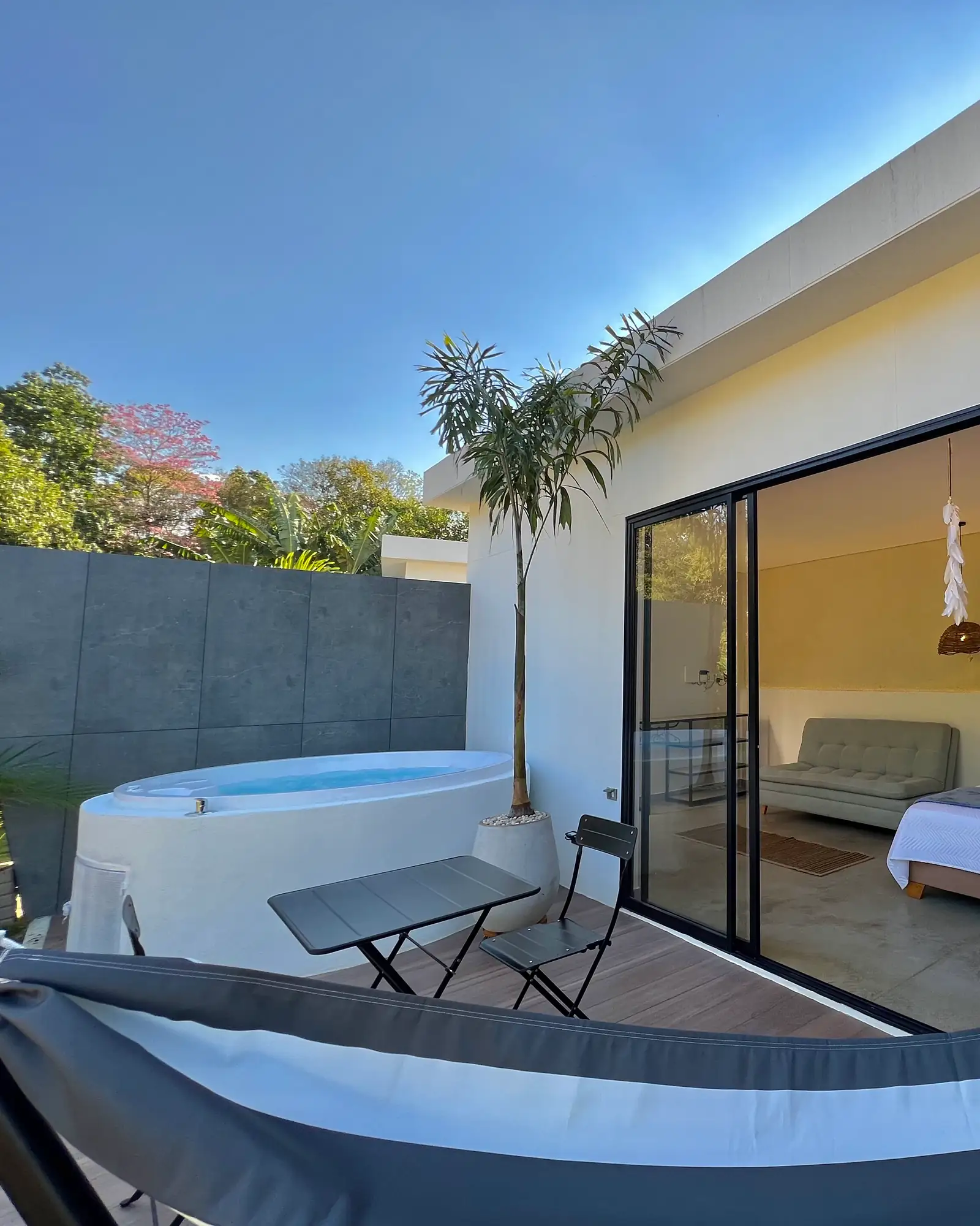 La hamaca en primer plano y el jacuzzi blanco al lado del ventanal de la cabaña